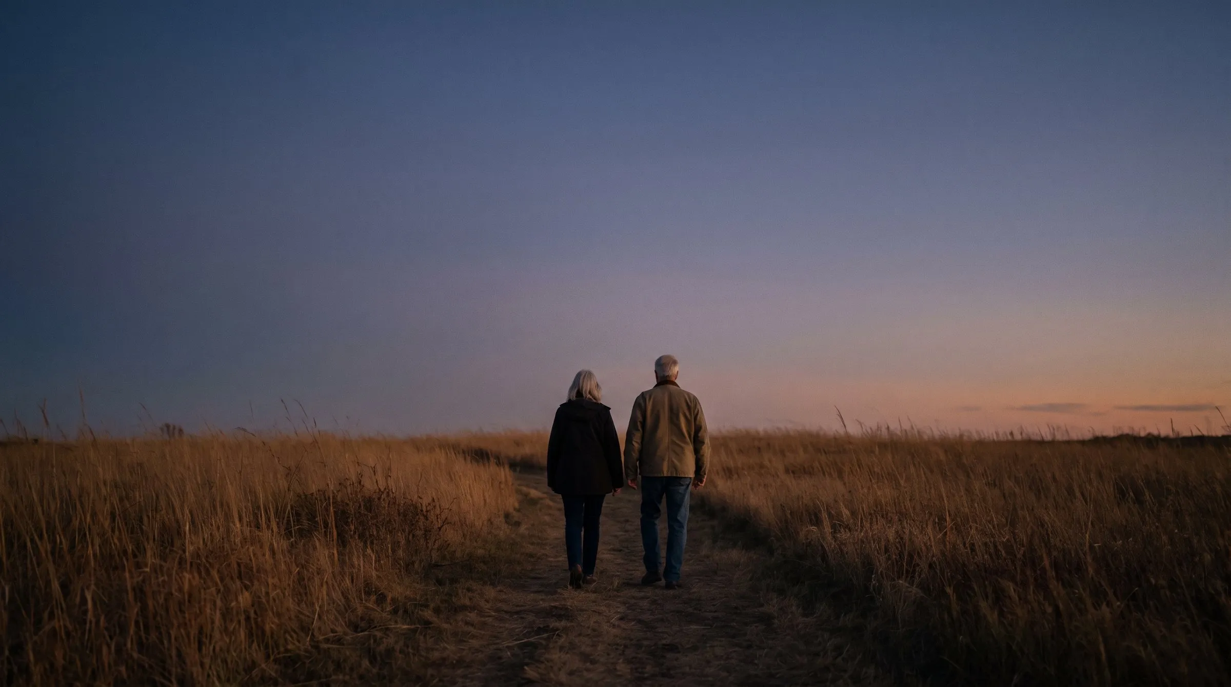 Two people walking a prairie path at dusk under a huge sky.