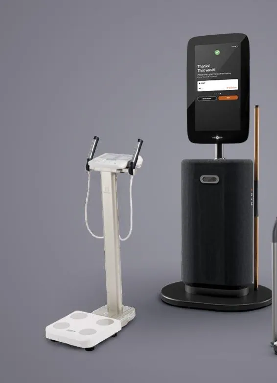 A body composition analyser with hand grips beside the EGYM Fitness Hub, a black column with a tall screen and a measuring pole.