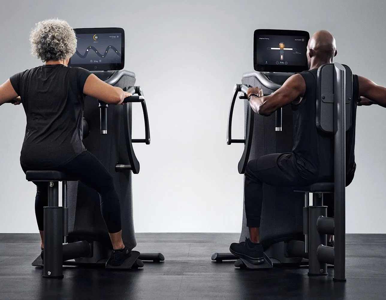 Two people train on EGYM Smart Strength machines, seen from behind, each following a curve on the machine's screen.